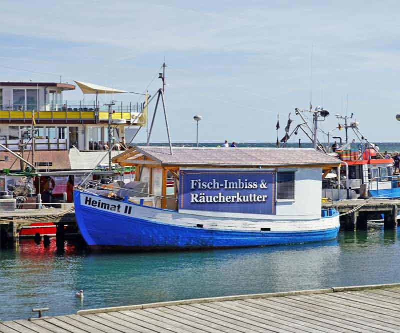 Fischkutter an einem sonnigen Tag im Hafen von Sassnitz, worauf Fischbrötchen an Gäste verkauft werden
